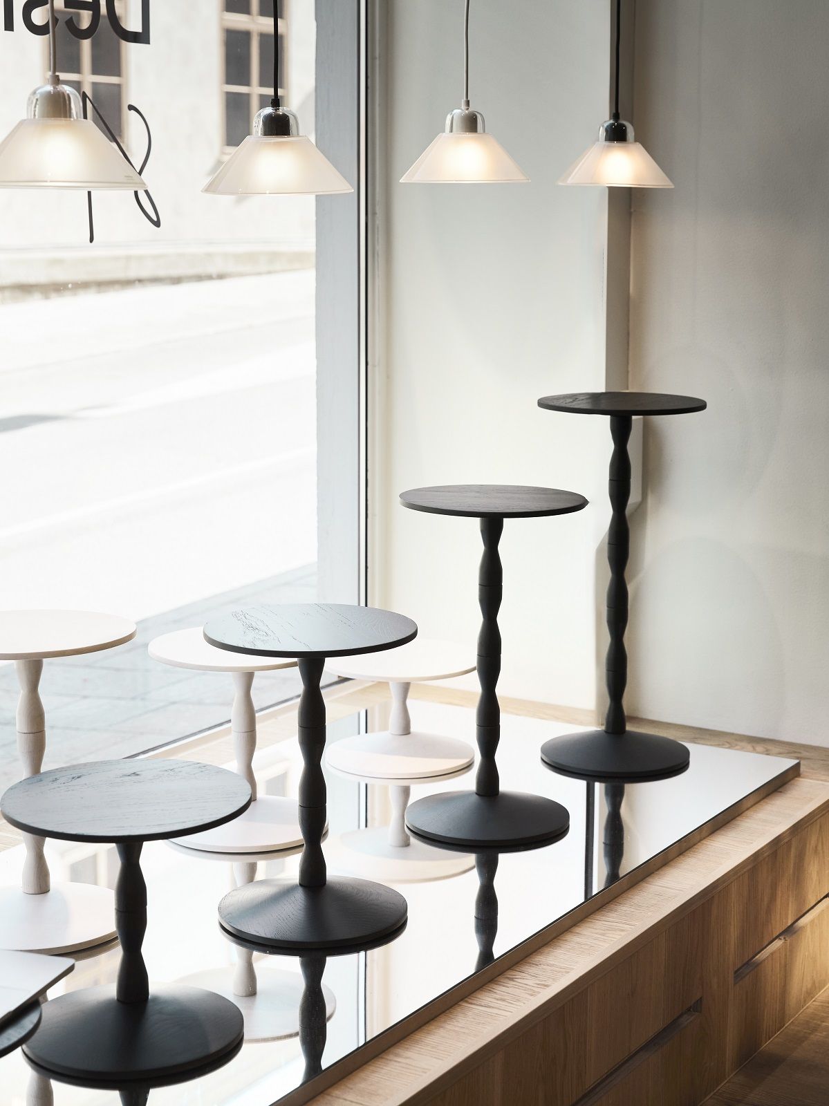 Mehrere Kalo Lamp Pendelleuchten von Design House Stockholm über runden Beistelltischen.