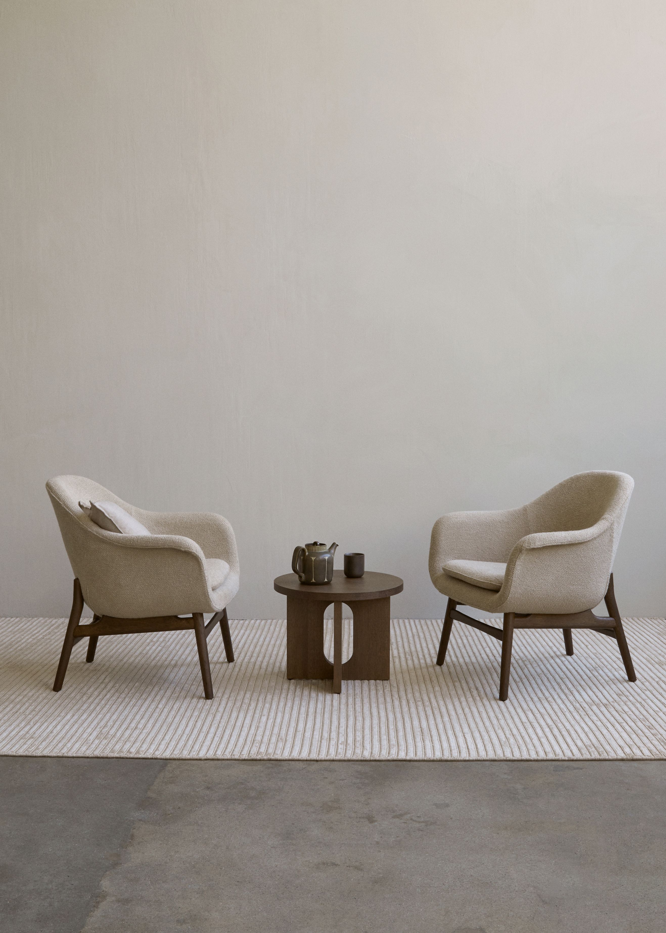 Androgyne Beistelltisch aus Walnuss von Audo zwischen zwei Sesseln auf einem Teppich.