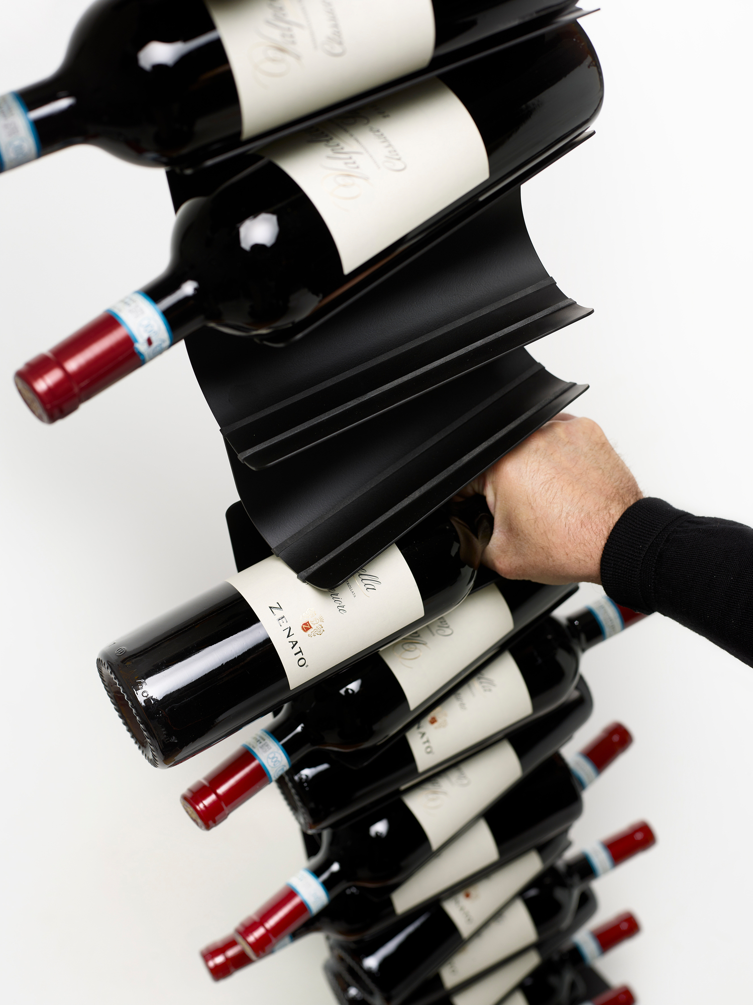Schwarzes Ptolomeo Vino Weinregal mit Weinflaschen, gehalten von einer Hand, modernes Weinregal Design.