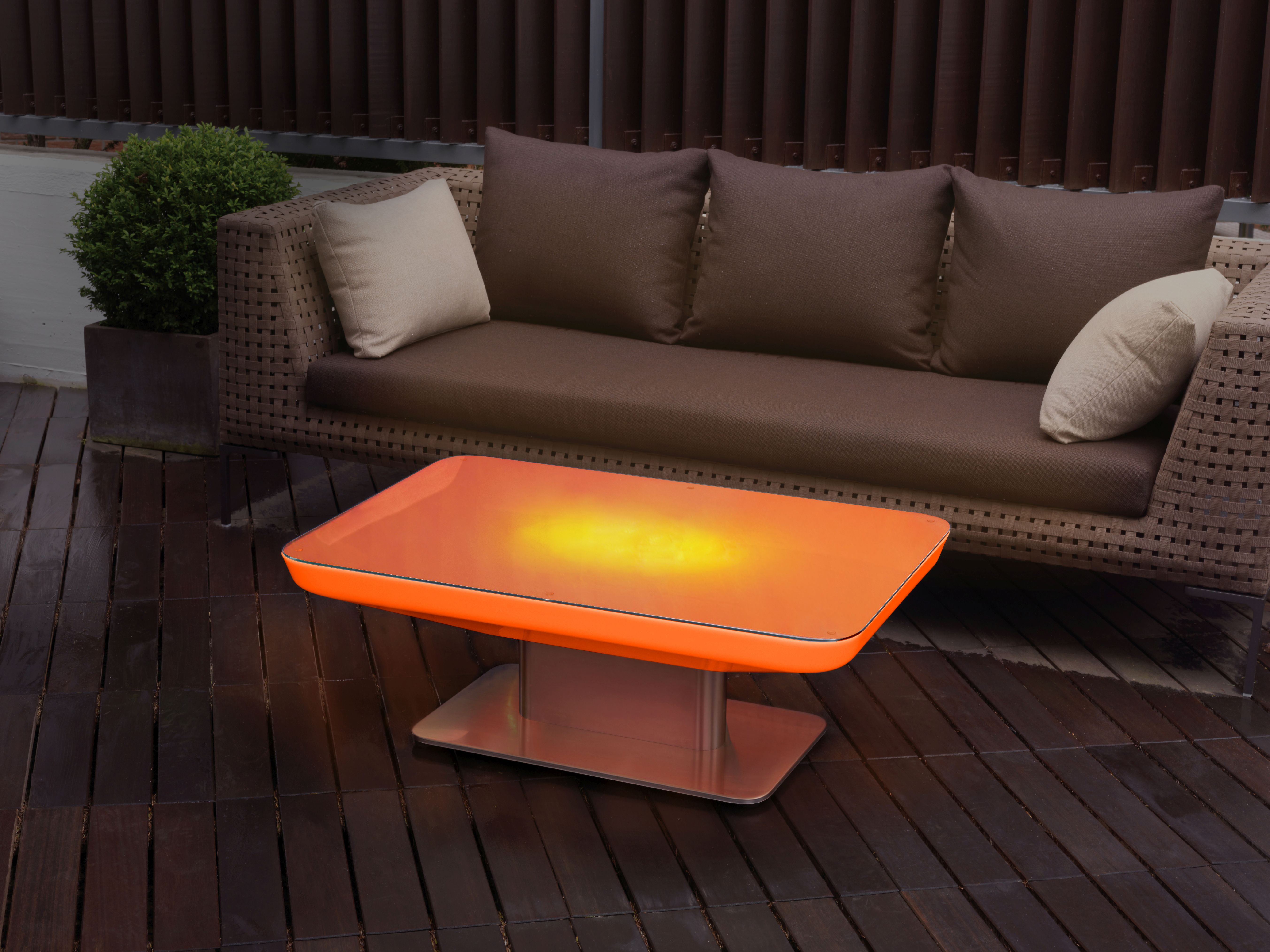 Moree Studio 36 LED Outdoor Tisch, orangefarben, leuchtend, mit Lounge-Möbeln im Hintergrund.