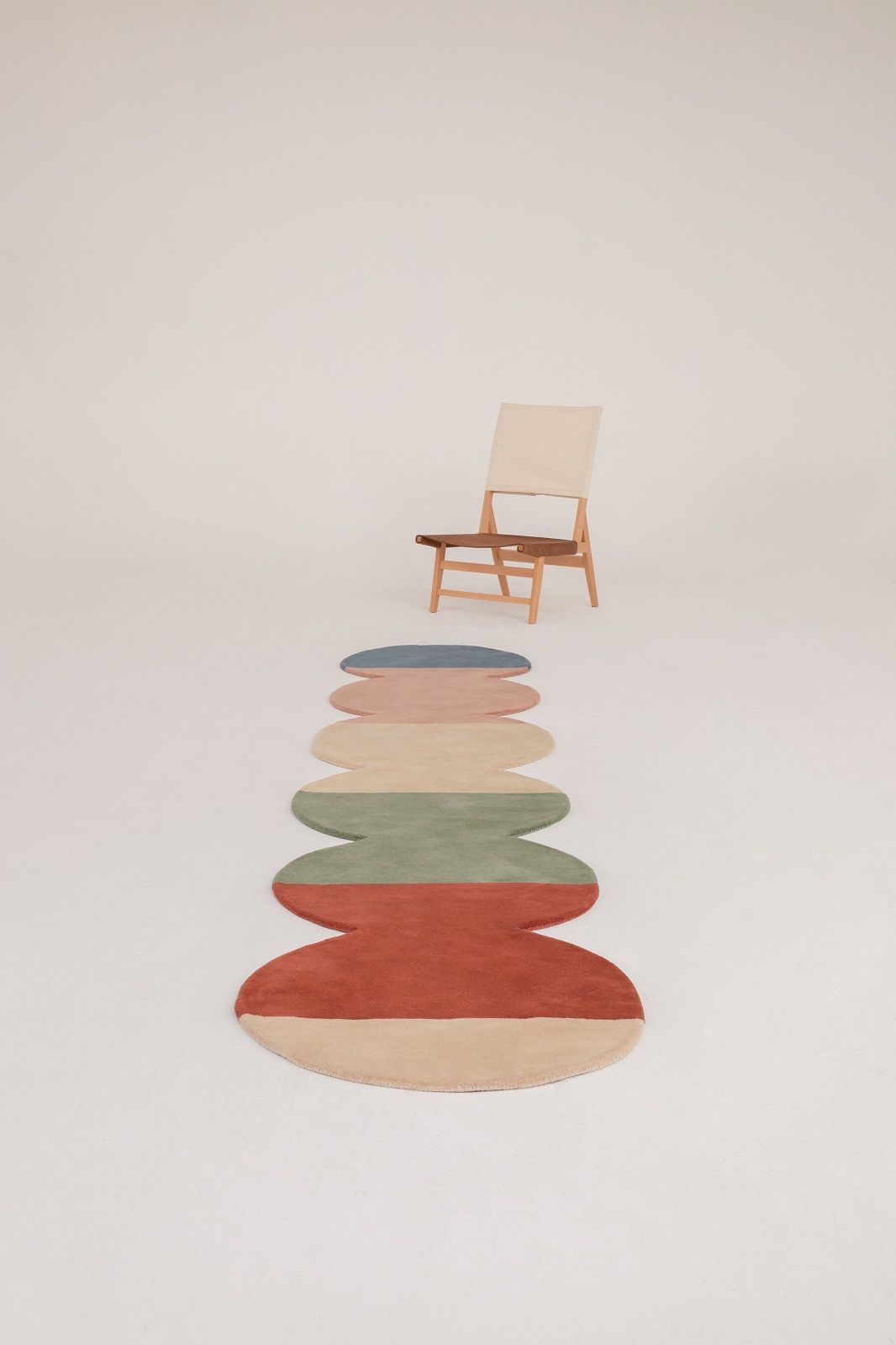 Nanimarquina Teppich "Pearls Runner" mit farbigen, runden Elementen und Stuhl im Hintergrund.