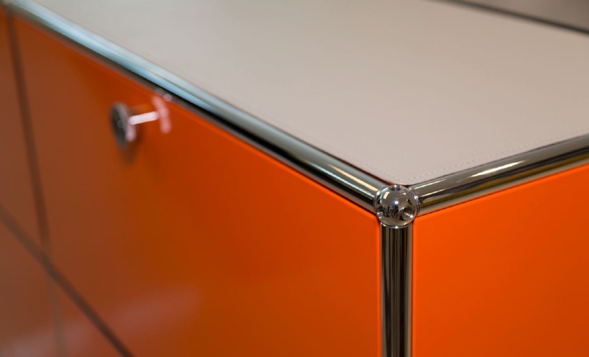 Detailaufnahme: Lichtgraue Lederauflage auf orangefarbenem USM Sideboard mit Chromgestell. Hochwertige Ledermatte für Möbel.