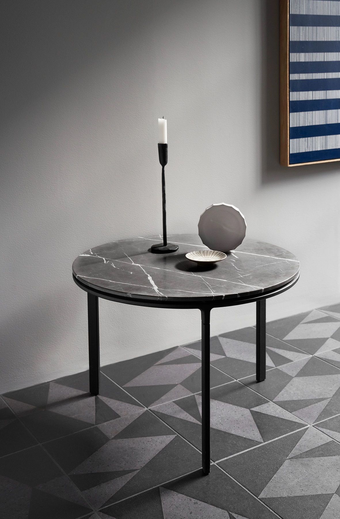 Runder Couchtisch Vipp Ø60 mit Marmorplatte und schwarzem Metallgestell, dekoriert mit Kerze und Keramik.