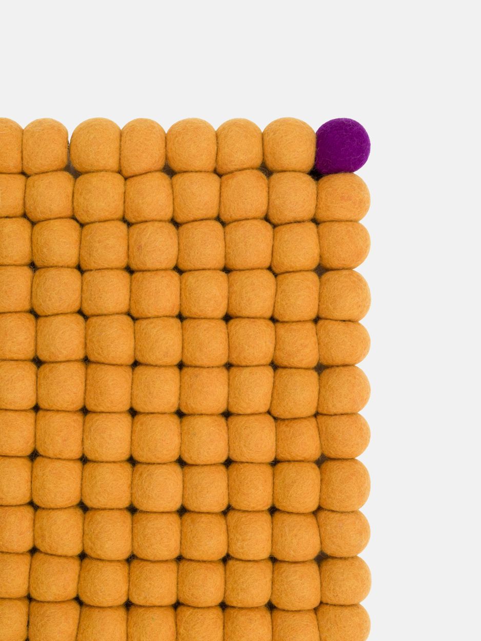 Detailansicht: Rechteckiger, goldgelber Filzteppich von myfelt, bestehend aus vielen Filzkugeln, mit einer violetten Kugel.