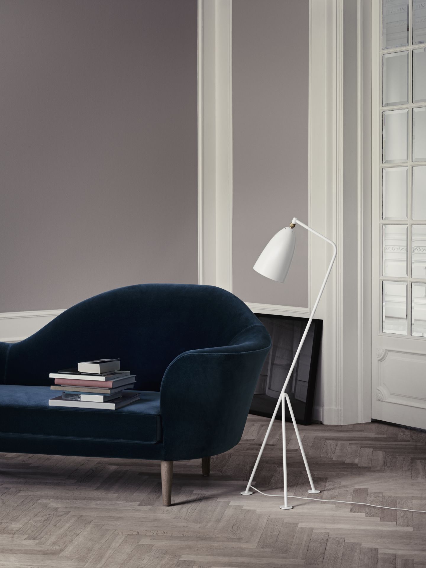 Weiße Gräshoppa Stehleuchte von Gubi neben blauem Sofa auf Parkettboden, modernes Wohnzimmer Design.