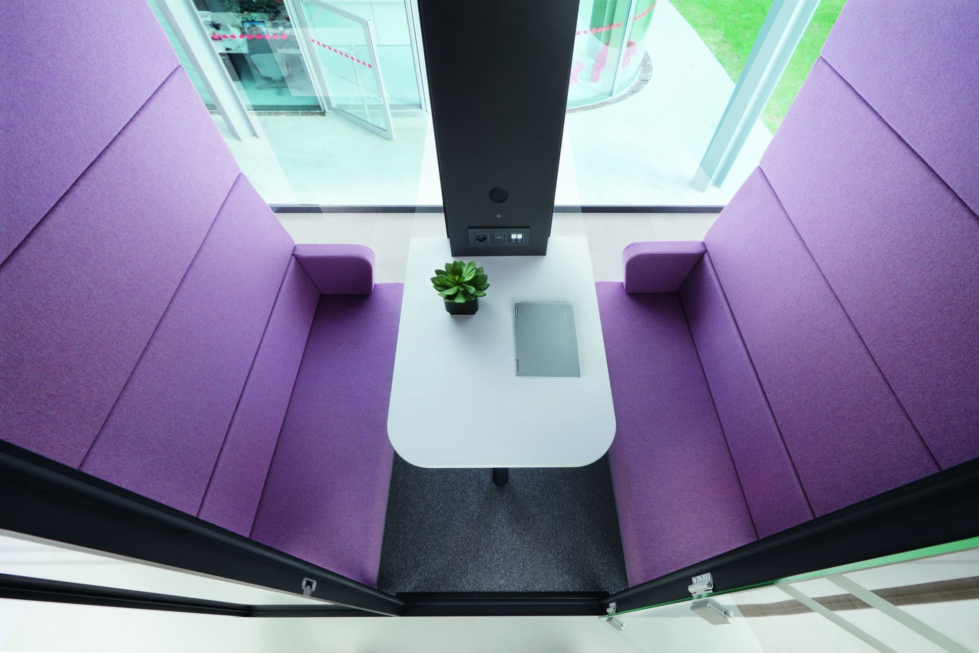 HushMeet Meetingbox: Innenansicht mit lila Sitzelementen, weißem Tisch und Laptop. Büro Besprechungsraum.