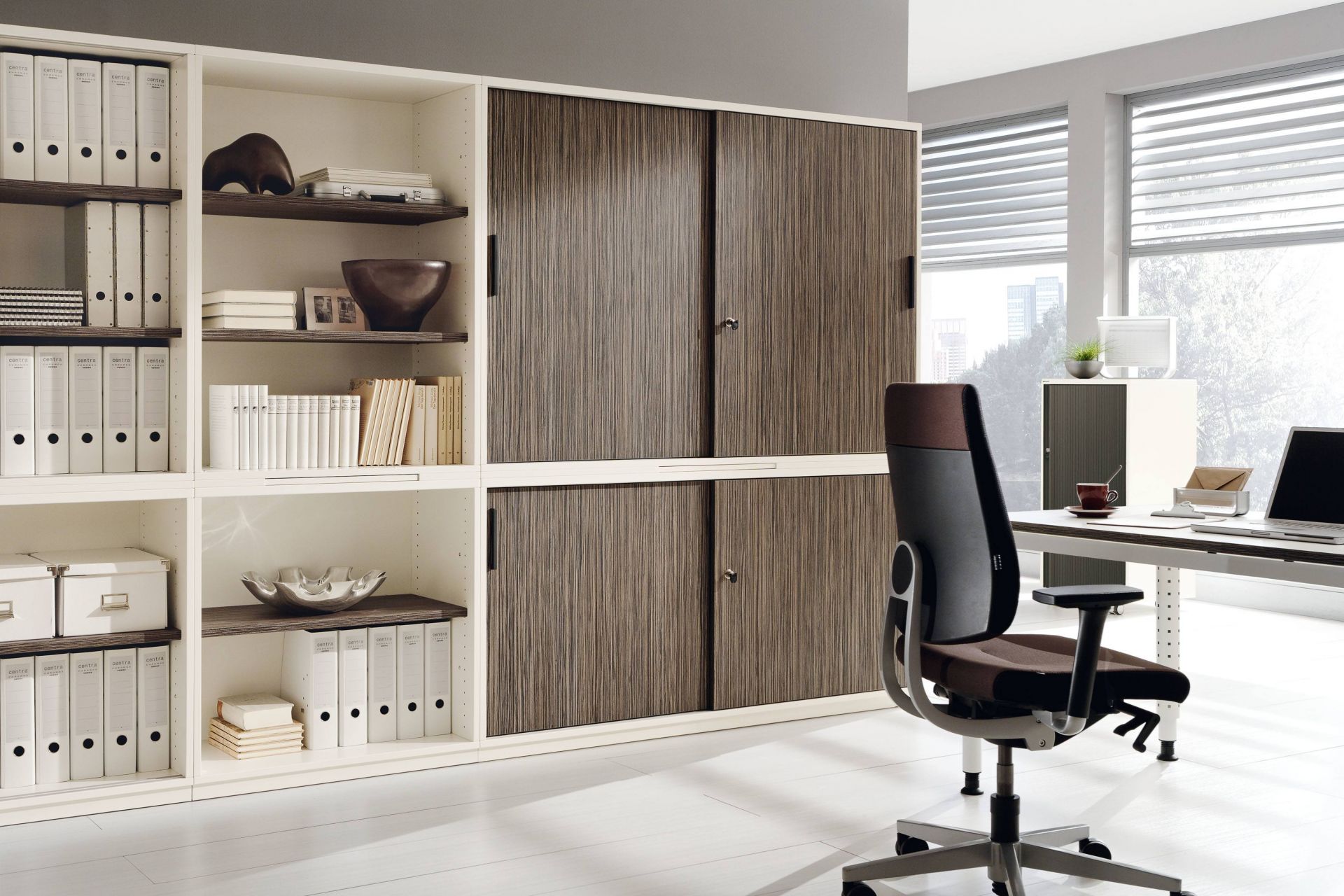 Büro mit Palmberg Querrollladenschrank Prisma 2, Regalen, Büromöbeln und Schreibtisch für moderne Arbeitsplatzgestaltung.