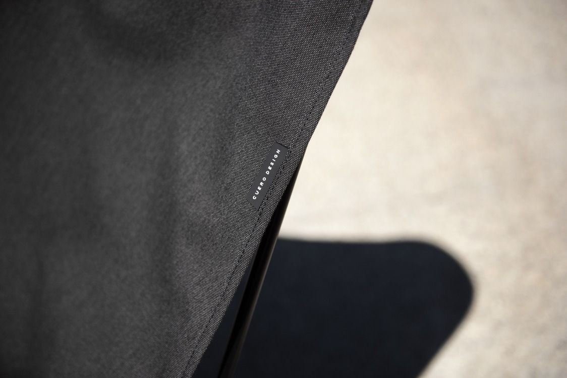 Detailaufnahme: Mariposa Outdoor Sessel Cuero Charcoal Pique mit Stoffstruktur und Markenlabel. Bequemer Outdoor-Sessel.