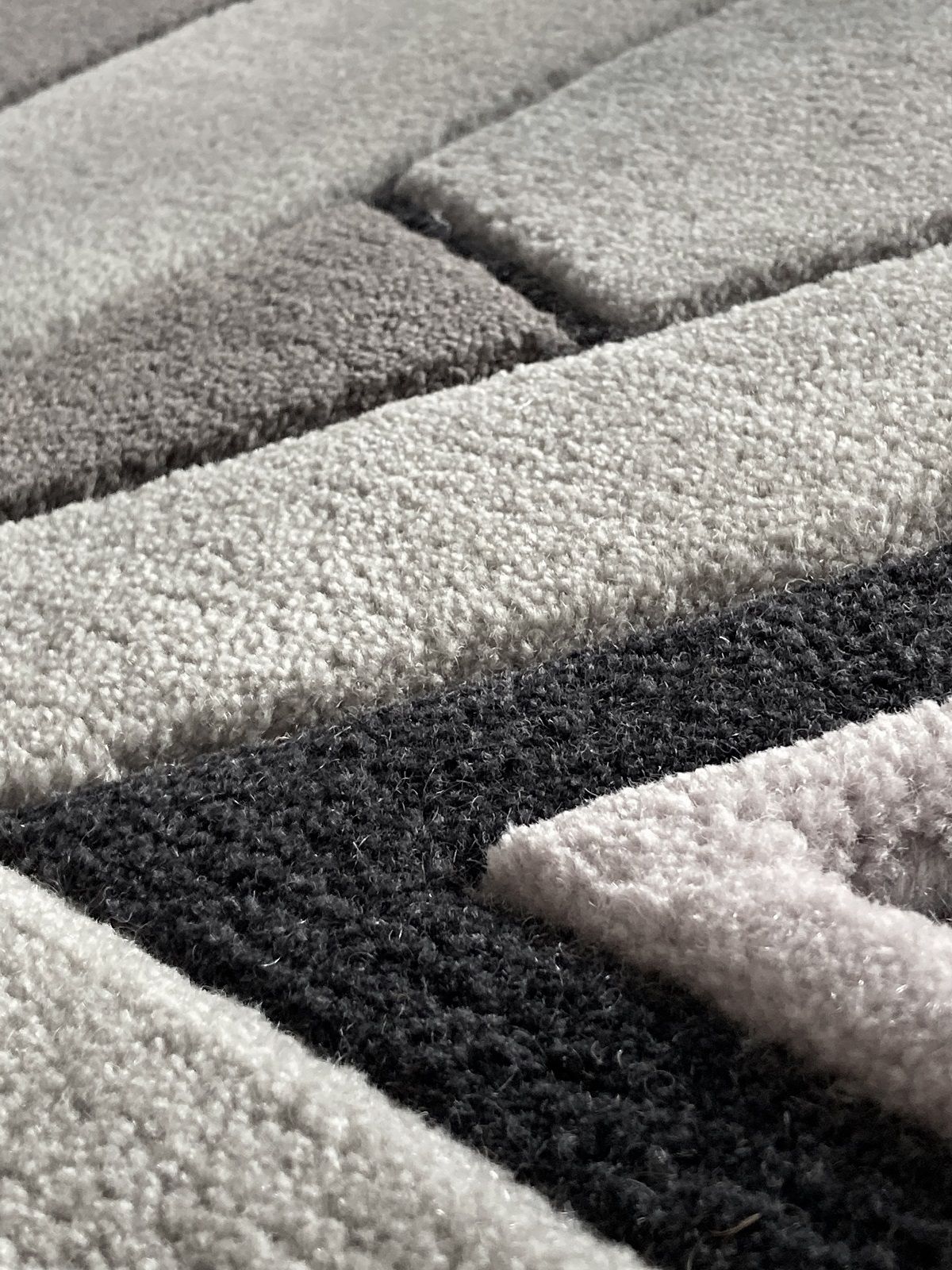 Detailaufnahme des grauen Hartô Teppichs Inès mit geometrischem Muster und weicher Textur.