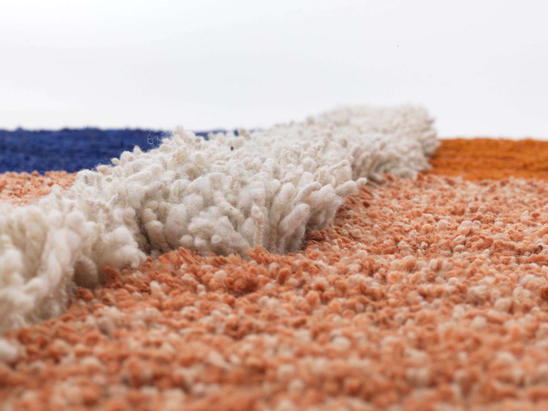 Detailaufnahme des Nudo Teppichs von Ames mit blauen, weißen und orangefarbenen Wollfasern.