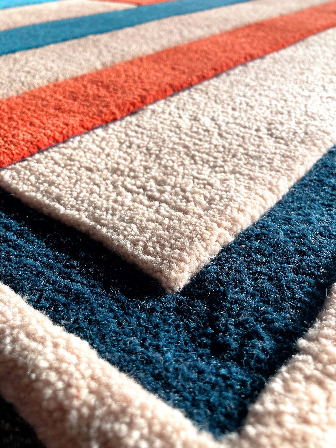 Detailaufnahme des Inès Teppichs von Hartô mit farbigen Streifen in Blau, Orange und Beige.