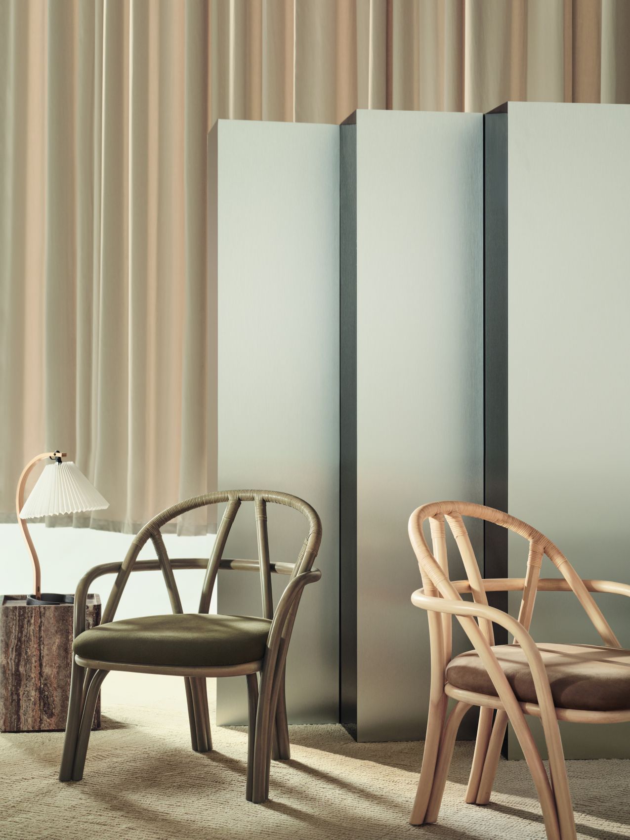 Nahaufnahme der Gubi Timberline Tischleuchte auf einem Holzhocker, neben zwei Rattanstühlen in einem stilvollen Interieur.