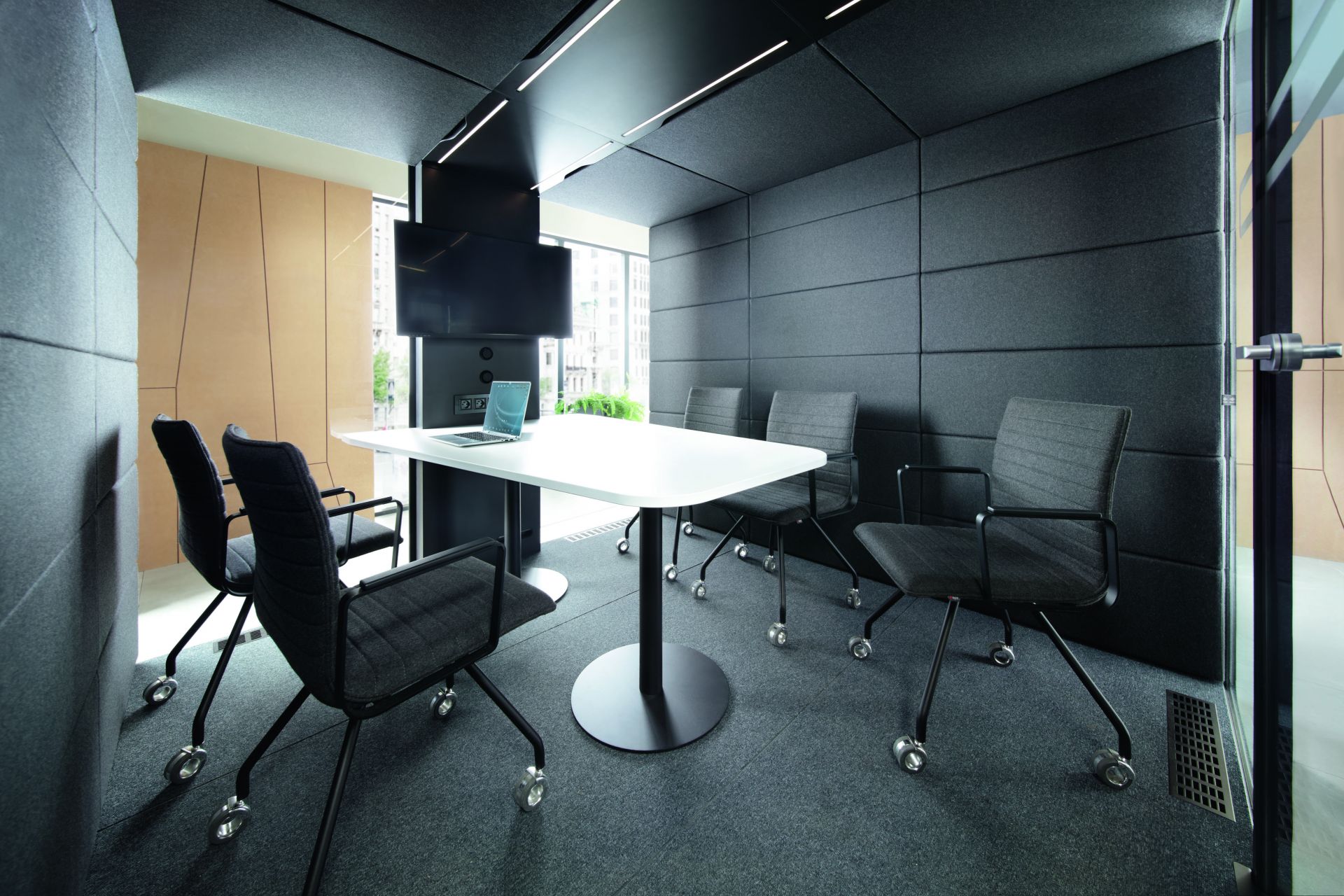 Modernes Büro mit weißem Konferenztisch, Laptop, grauen Bürostühlen mit Rollen und Akustikpaneelen.